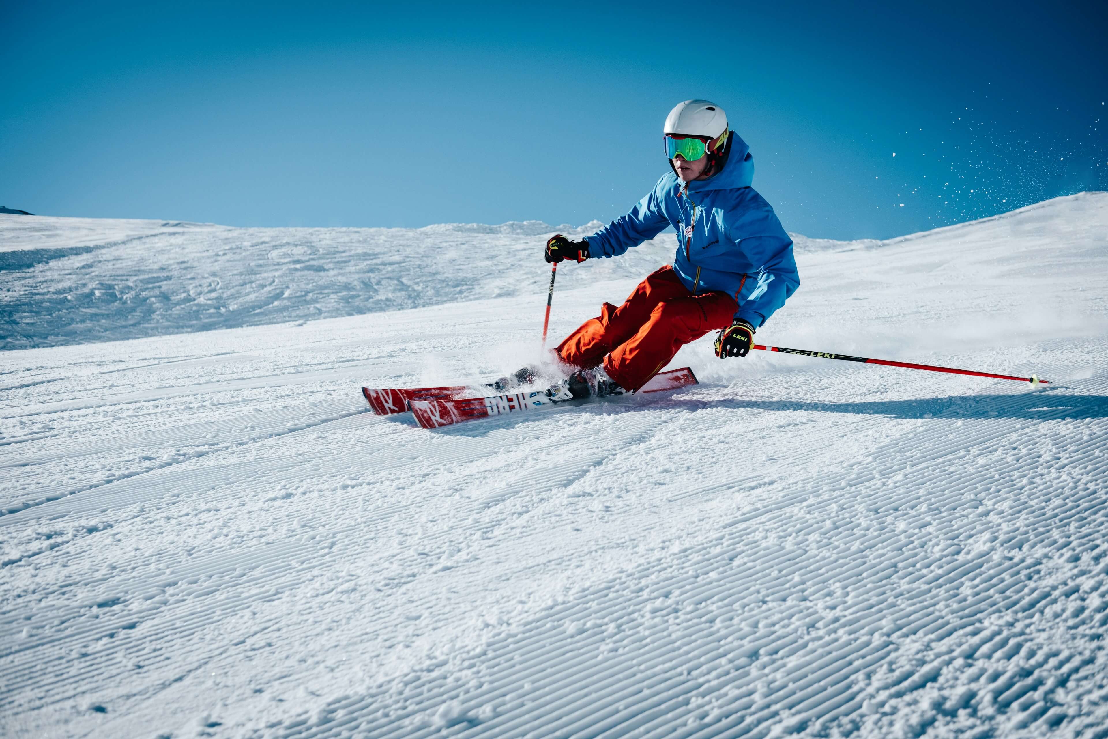 A skier carving down a groomed slope under a blue sky